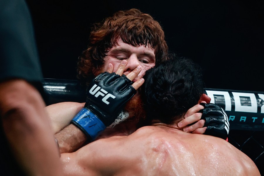 Michel Pereira pressing Shara Magomedov to the cage and has one his hands over his mouth, touching squeezing his nose